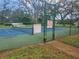 Tennis court rules are displayed at the entrance to the fenced court with trees in the background at 12119 Sunny Glen Ln # G2, Hudson, FL 34669