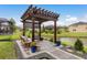 A wood pergola that overlooks the lake with comfortable seating and beautiful landscaping at 1771 Whitewillow Dr, Wesley Chapel, FL 33543