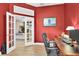 Home office featuring red walls, wood floors, desk with computer, and french doors to living area at 18328 Treehaven Dr, Hudson, FL 34667