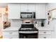 Close up of kitchen appliances, including a microwave, stove and oven, surrounded by white countertops and cabinets at 3013 Appleblossom Trl, Spring Hill, FL 34606