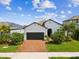 Charming single-story home featuring a brick driveway, lush landscaping, and a welcoming black garage door at 6229 Sea Air Dr, Apollo Beach, FL 33572