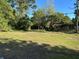 A spacious grassy front yard surrounded by lush trees leads to a cozy single-story home at 8711 Cutlass Dr, Hudson, FL 34667