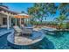 Resort-style pool area with a fire pit, jacuzzi, lounge chairs, and umbrella with views of lush landscaping at 10019 Milano Dr, Trinity, FL 34655