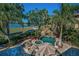 Aerial view of a swimming pool with stone waterfall, hot tub, fire pit, and landscaping overlooking the lake at 10019 Milano Dr, Trinity, FL 34655