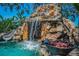 Backyard pool featuring a rock waterfall, slide, and fire pit with lush foliage and a blue sky backdrop at 10019 Milano Dr, Trinity, FL 34655