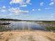 Scenic lake view showcasing a boat dock, sandy shoreline, lily pads, and blue sky with clouds at 11630 Pasadena Rd, Dade City, FL 33525