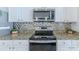 Close-up of the kitchen's stainless steel stove and microwave, granite counters, and stylish tile backsplash at 13160 Golden Lime Ave, Spring Hill, FL 34609