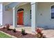 Inviting front porch with a bright red door, elegant columns, and manicured landscaping at 13741 Judy Ave, Hudson, FL 34667