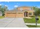 Inviting tan two-story home featuring a well-manicured lawn, three-car garage, and charming front-yard landscaping at 4335 Canongate Ct, Spring Hill, FL 34609