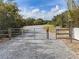 Gated community entrance with gravel road surrounded by mature trees under a blue sky with clouds at 6109 Japonica Ct, New Port Richey, FL 34655