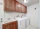 A practical laundry area that includes a utility sink, washer, dryer, and wooden cabinets at 7700 Fairlawn Dr, Hudson, FL 34667