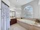 Bright bathroom features a large soaking tub under a large window, vanity with wood cabinets, and tiled floors at 8523 Regal Ln, Hudson, FL 34667
