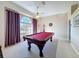 Game room showcasing a plush red pool table, carpet, a ceiling fan, and a large window with draped curtains at 8523 Regal Ln, Hudson, FL 34667