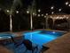 Backyard pool and spa with brick deck, string lights, palm trees and covered pergola at nighttime at 3555 Bracknell Ct, Land O Lakes, FL 34638