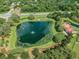 Aerial view of a pond with a fountain, a barn, and surrounding mature trees and a road at 8635 Creedmoor Ln, New Port Richey, FL 34654