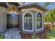 Elegant front entrance with arched windows, a dark wood door, and landscaped garden beds at 12800 Solola Way, Trinity, FL 34655