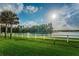 Lakeside view with a white fence in the foreground, showing a calm pond and distant trees under a sunny sky at 12800 Solola Way, Trinity, FL 34655