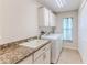 Bright laundry room featuring a utility sink with granite countertops, washer, dryer, and white cabinets at 4044 Chesterfield Dr, Spring Hill, FL 34609