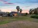 Expansive backyard featuring lush green grass, mature trees and screened-in patio with outdoor lighting at sunset at 4423 Gevalia Dr, Brooksville, FL 34604