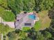 Aerial view of a home with a pool, solar panels, brick driveway, and lush landscaping offering privacy at 18502 Winding Oaks Blvd, Hudson, FL 34667