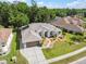 An aerial view of a beige single-Gathering home featuring a manicured lawn, an attached two-car garage, and a shingled roof at 4080 Gevalia Dr, Brooksville, FL 34604