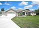 Inviting one-story home featuring a well-manicured lawn and a three-car garage with white doors at 7495 Birdland Cres, Spring Hill, FL 34607