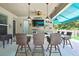 Relax in this outdoor kitchen featuring bar seating, granite countertops, a ceiling fan, and a TV for entertainment at 7495 Birdland Cres, Spring Hill, FL 34607