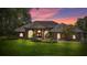 Charming brick home at twilight featuring arched windows, lush landscaping, and a well-maintained lawn at 888 Royal Birkdale Dr, Tarpon Springs, FL 34688