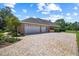 View of the home's three-car garage and brick-paved driveway, surrounded by lush landscaping at 888 Royal Birkdale Dr, Tarpon Springs, FL 34688