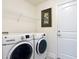 Clean laundry room features a white washer and dryer, overhead wire shelf, and a decorative piece of artwork at 13111 Precept Way, Hudson, FL 34669