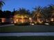 Exterior home elevation at night featuring exterior uplighting and tropical landscaping at 663 Turnberry Ct, Tarpon Springs, FL 34688