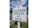 Humorous community sign that reads, 'Caution Adults at Play', set against a blue sky and trees at 1006 Sweet Jasmine Dr, Trinity, FL 34655