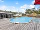 Well-maintained above-ground pool with wooden deck, steps, lounge chairs, and a partially-covered patio on a bright day at 13052 Drysdale St, Spring Hill, FL 34609