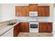 Functional kitchen featuring wood cabinetry, white appliances, and granite countertops at 13618 Niti Dr, Hudson, FL 34669