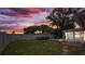 Fenced backyard with green grass, mature trees and a vibrant sunset sky at 3638 Bigelow Dr, Holiday, FL 34691