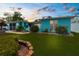 Charming turquoise home with a lush green lawn and vibrant flowerbeds beneath a colorful sky at 9015 Mark Twain Ln, Port Richey, FL 34668