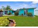 Charming turquoise home with a lush green lawn and vibrant flowerbeds beneath a colorful sky at 9015 Mark Twain Ln, Port Richey, FL 34668