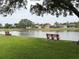 Scenic pond view showcasing benches, lush green lawn, and homes in the background at 1121 Riveredge Dr, Tarpon Springs, FL 34689