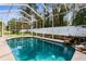Sun-drenched screened-in pool area with waterfall feature and landscaped surroundings at 11443 Marsh Creek Ct, New Port Richey, FL 34654