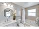 Bright bathroom featuring a round mirror, white vanity, and bathtub with light beige tile surround at 1486 Loman Ct, Palm Harbor, FL 34683