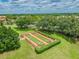 Aerial view of a bocce ball court surrounded by a green hedge with tables and umbrellas for onlookers at 18418 Bent Pine Dr, Hudson, FL 34667