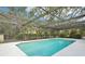 An in-ground screened pool surrounded by a white tile and a mature treed backyard at 18633 Oak Way Dr, Hudson, FL 34667