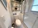 Bright bathroom features a toilet, shelving unit with decorations, and walk-in shower with textured glass at 9311 Haas Dr, Hudson, FL 34669