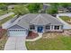 Aerial view of a well-maintained home with a large driveway, landscaped yard, and a charming blue front door at 1219 Aladdin Rd, Spring Hill, FL 34609