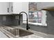 Close up of modern sink with black faucet, gray backsplash, marbled countertop, and a window overlooking backyard at 13411 Lisa Dr, Hudson, FL 34667