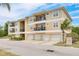 Exterior shot of a tan condo building with balconies and garages surrounded by lush green landscaping at 5041 Royal Palms Way # 203, New Port Richey, FL 34652