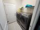 The laundry room has gray washer and dryer, white door, and shelf for storage at 954 Old Windsor Way, Spring Hill, FL 34609