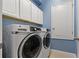 Well-equipped laundry room with modern white washer and dryer, complemented by overhead storage cabinets at 11401 Quiet Forest Dr, Tampa, FL 33635