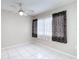 Bedroom featuring white tile flooring, neutral walls, and window with decorative dark patterned curtains and a ceiling fan at 13003 Sandburst Ln, Hudson, FL 34667