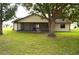 Backyard view featuring the home, screened in porch, lush green grass, and large shade trees at 13425 Bonita Ave, Spring Hill, FL 34609